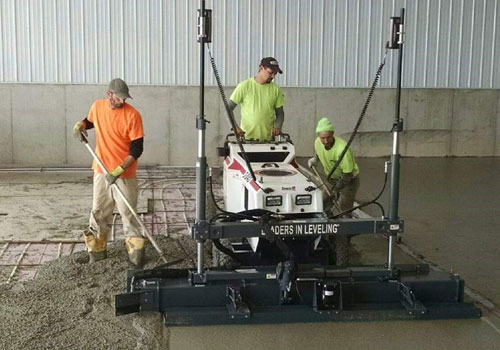 Team of workers from Van Haren Construction using a power concrete screed to flatten and smooth freshly poured concrete over rebar for a commercial shed floor